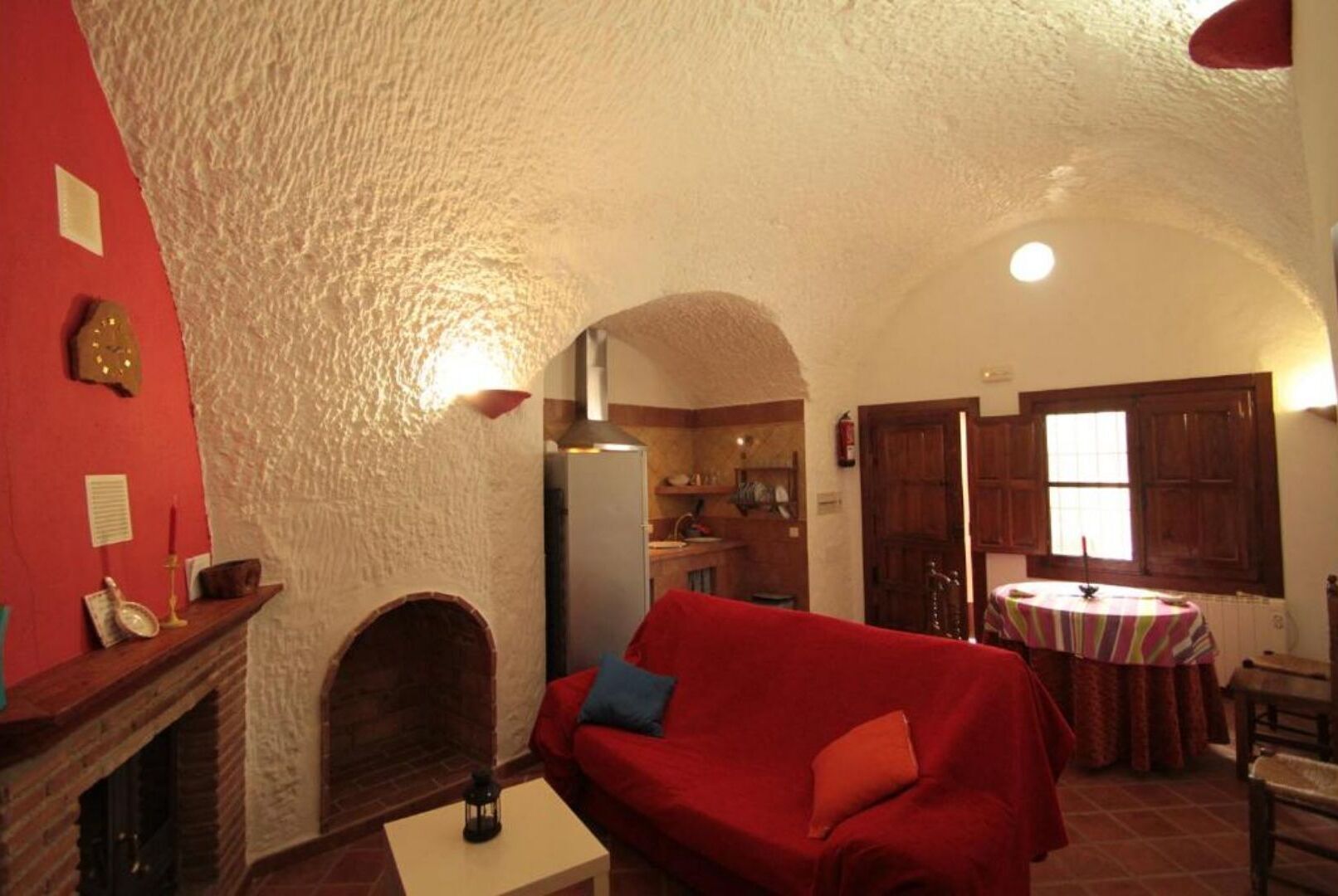 A cozy living room with a red sofa, a fireplace, and a kitchen visible through an archway.