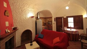 A cozy living room with a red sofa, a fireplace, and a kitchen visible through an archway. - Las Chumberas Cave - Los Cerezos (Benalua)