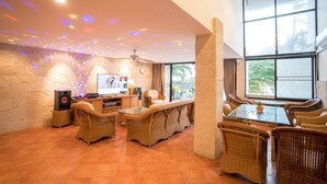 A spacious living area with a flat-screen TV, wicker furniture, and a large window offering a view of the outdoors. - Dojo pool villa beach front and sea view (Unknown)