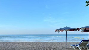 A beach with sand, a clear sky, and two umbrellas providing shade. - Dojo pool villa beach front and sea view (Unknown)