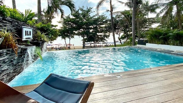 A poolside area with a lounge chair, a stone wall, and palm trees. - Dojo pool villa beach front and sea view (Unknown)