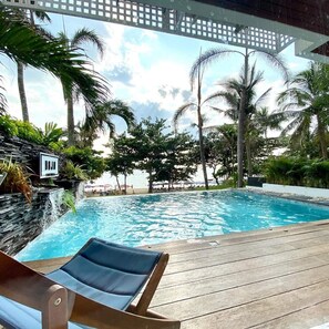 Un espace aménagé au bord de la piscine, avec un fauteuil de relaxation, un mur en pierre et des palmiers.