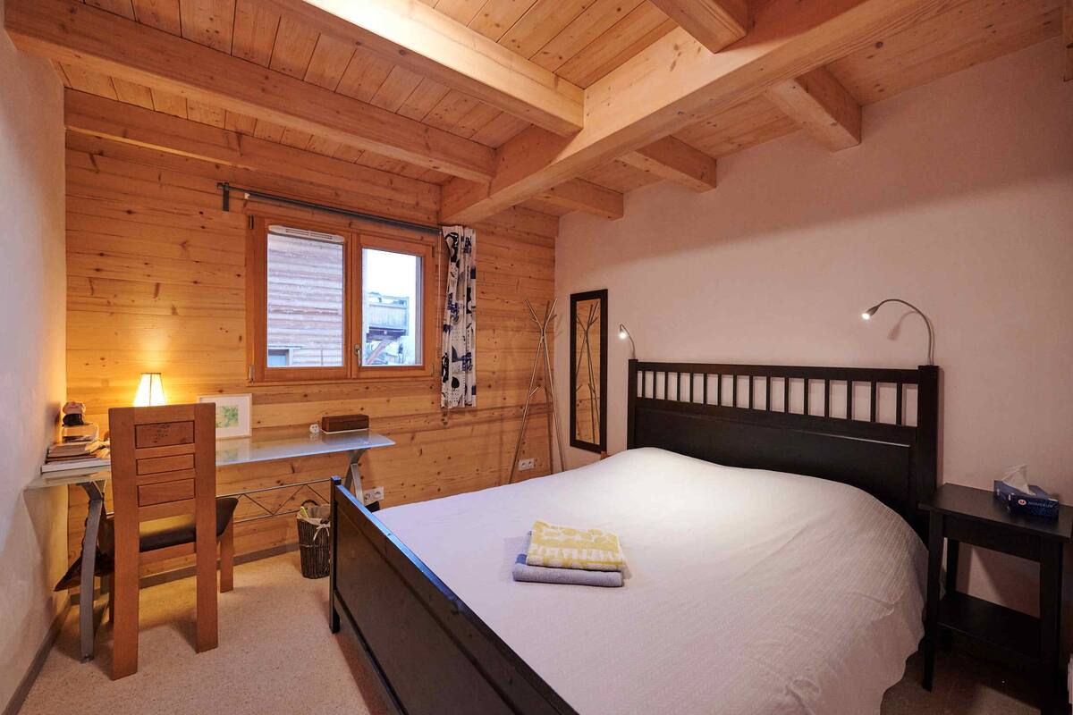 Ein Zimmer mit Holzwänden, ausgestattet mit einem Bett, einem Schreibtisch, einem Stuhl und einem Fenster mit Vorhängen.