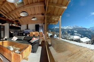 Un interior moderno con techo de madera, una mesa de comedor de vidrio y vistas a montañas nevadas.