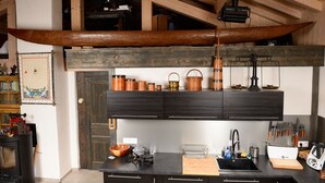 A kitchen with a wooden canoe suspended above the counter, a black countertop, and various kitchen utensils and appliances. - B&B - La Case A Kio Bourg-St-Maurice Les Arcs (Les Chapelles)