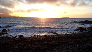 Una playa con rocas y olas al atardecer.