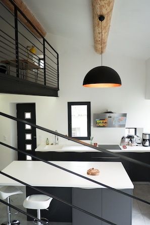 Cozinha moderna com ilha central, guarda-corro preto e luminária pendente.
