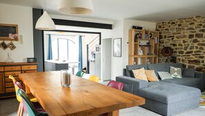 A modern living room with a grey sofa, wooden dining table, colorful chairs, and a stone accent wall. - La Grange 1832 - 10 mins from Aubenas (Saint-Étienne-de-Boulogne)