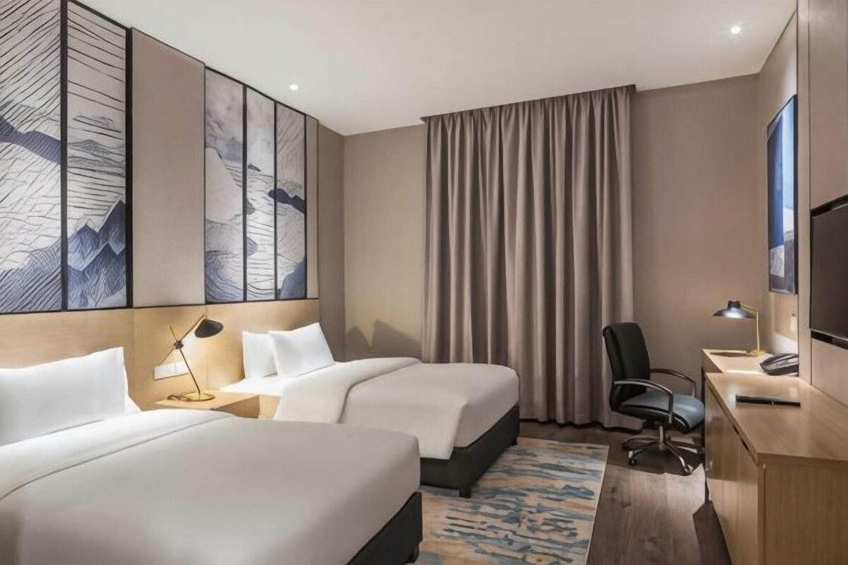 A hotel room with two beds, a desk with a computer, a chair, and a large artwork on the wall.