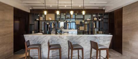 A modern kitchen with a marble island, bar stools, pendant lighting, and a built-in shelving unit.