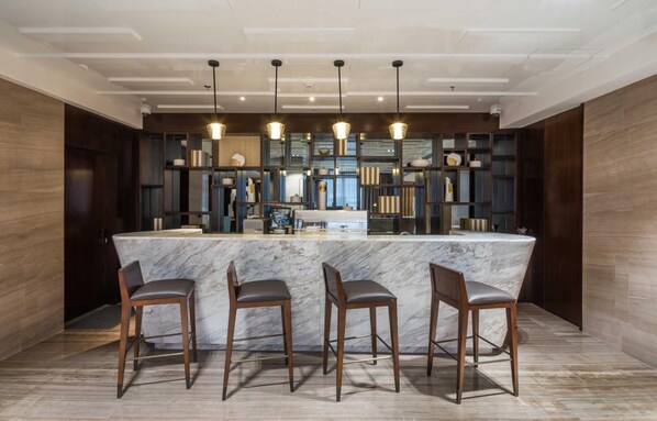Una cocina moderna con una isla de mármol, taburetes de bar, iluminación colgante y una estantería empotrada.
