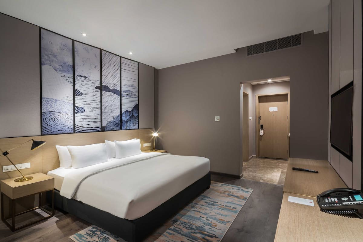 A modern hotel room with a large bed, bedside tables, a flat-screen TV, and a large abstract artwork on the wall.