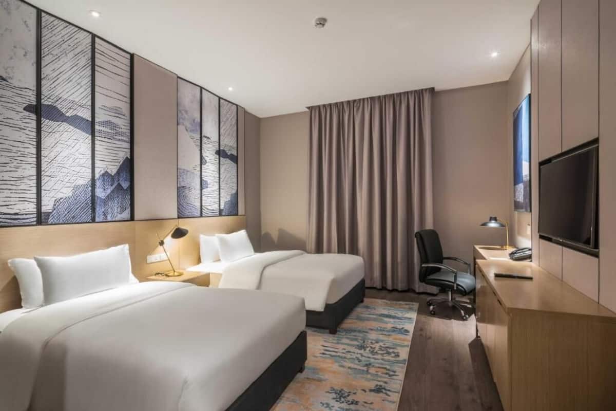 A hotel room with two beds, a desk, a chair, a TV, and artwork on the walls.
