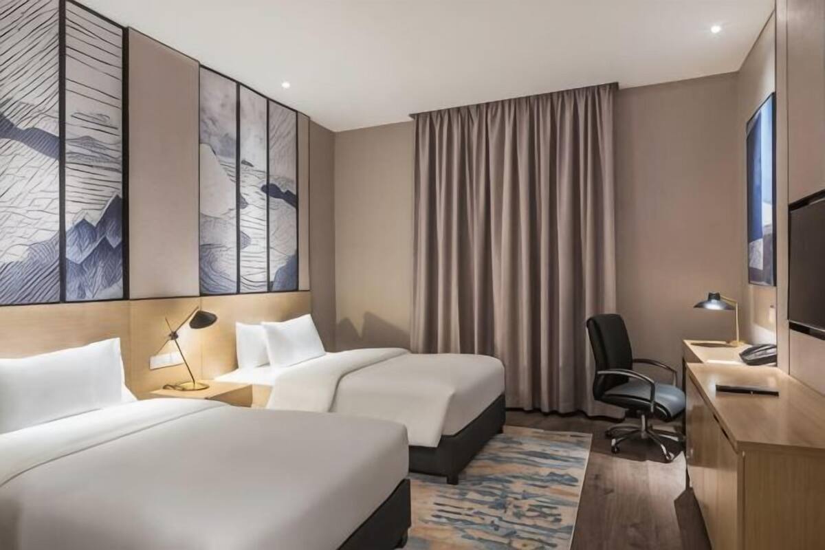 A hotel room with two beds, a desk with a computer, a chair, and a large artwork on the wall.
