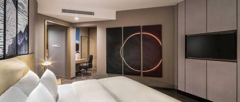 A modern hotel room with a large bed, a flat-screen TV mounted on the wall, and a unique circular artwork above the bed.