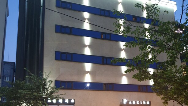 Un hotel amb façana moderna, senyalització il·luminada i una zona d'aparcament.