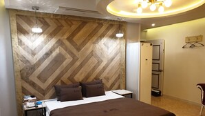 Habitació d'hotel amb un capçal de llit amb dibuix de guia de cuc, un llit amb edredó marró, taules de nit amb un telèfon i comandament a distància, i una làmpada penjant.