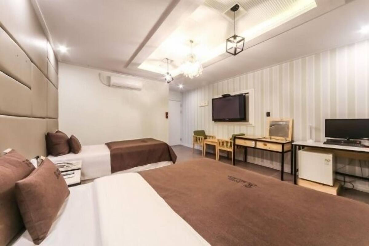 A hotel room with two beds, a desk, a chair, a television, and a minibar.