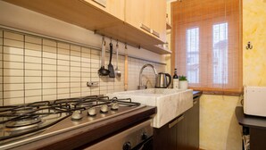 Een keuken met een gasfornuis, een spoelbak, houten kastjes en een raam met zonwering.