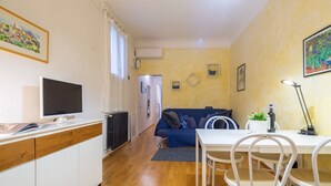 Een ruimtelijk ingerichte leefruimte met een kitchenette, een eethoek, een bank en een televisie.