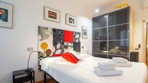 Een moderne hotelkamer met een groot bed, een nachtkastje, een kledingkast en kunstwerken in lijsten aan de muur.