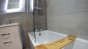 Une salle de bain moderne avec une baignoire, un tapis de bain en bois et un meuble-lavabo blanc doté de tiroirs.
