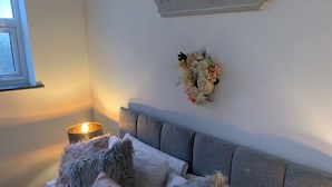 Une chambre à coucher avec un lit, une table de chevet sur laquelle est posée une bougie, un panneau décoratif au mur et une décoration florale.