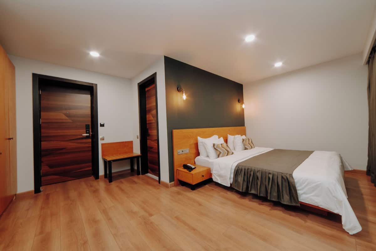 A modern bedroom with a wooden floor, a bed with a headboard, a nightstand, a bench, and a door.