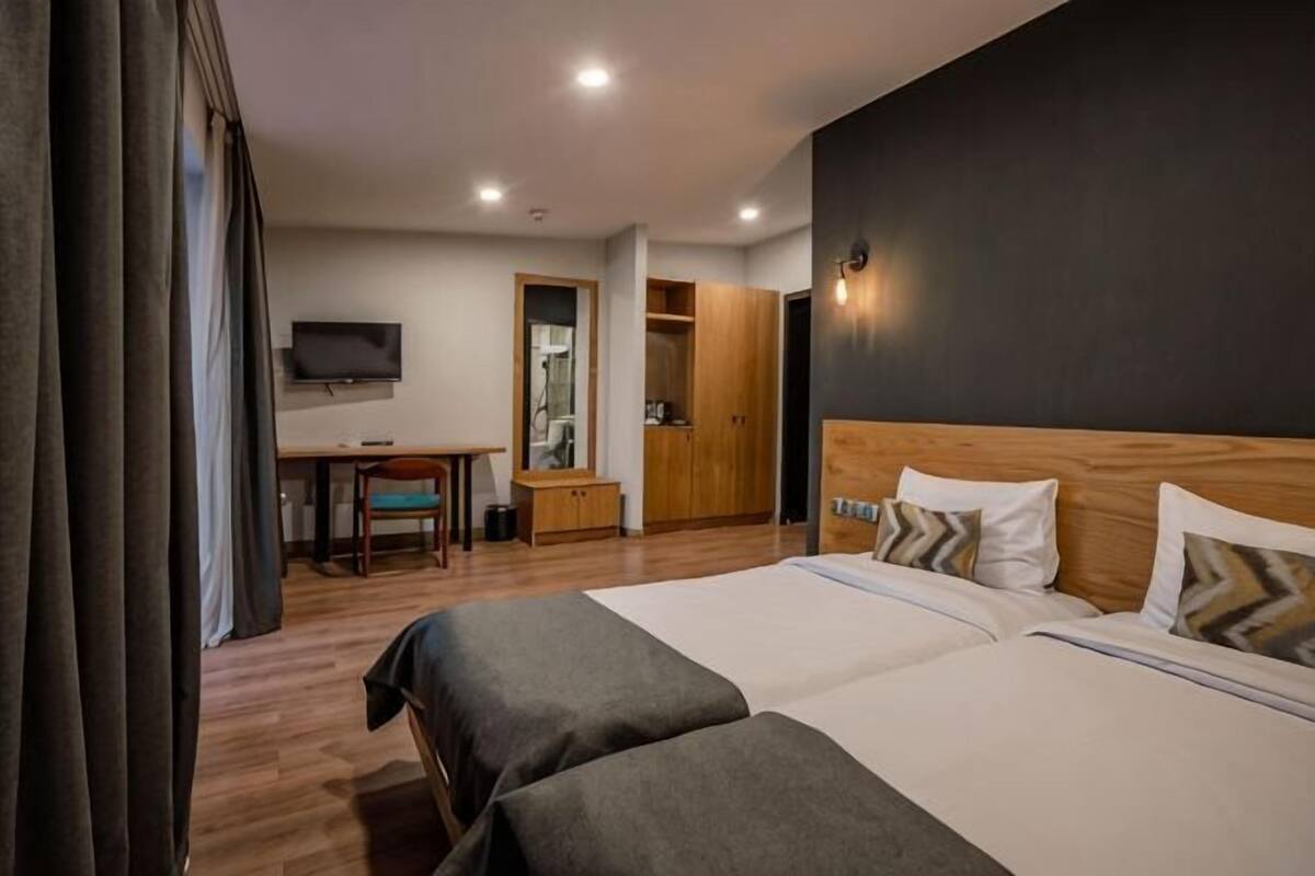 A hotel room with two beds, a desk, a TV, a wardrobe, and a mirror.