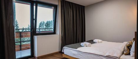 Habitación de hotel con cama, ventana con cortinas, piso de madera y una lámpara en el techo.
