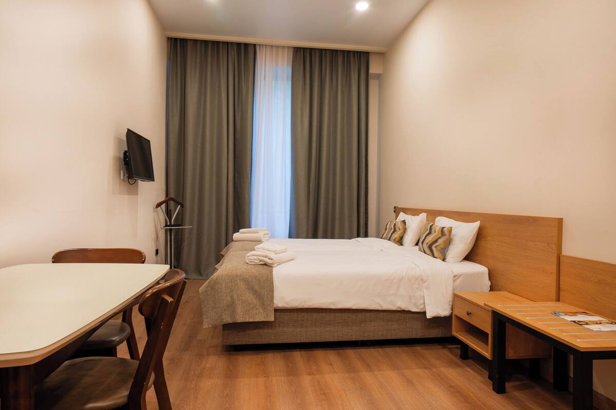 A hotel room with a bed, a desk, a chair, and a TV on the wall.