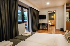 A hotel room with a large bed, a desk, a chair, a TV, and a view of the outdoors.