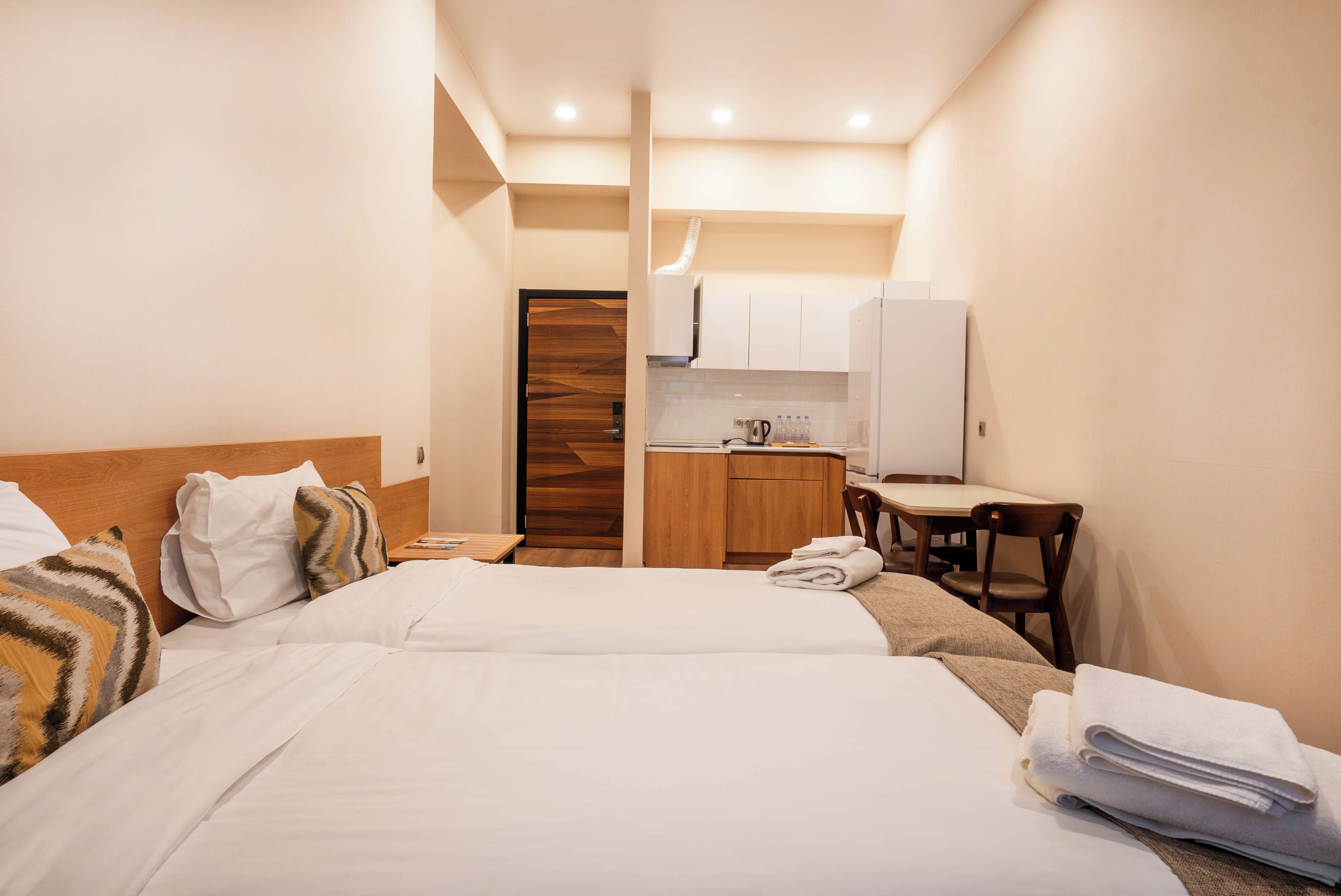 A hotel room with two beds, a kitchenette, and a small dining area.