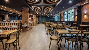 Um restaurante amplo com mesas e cadeiras de madeira altas, detalhes em tijolo e janelas grandes que oferecem vistas.