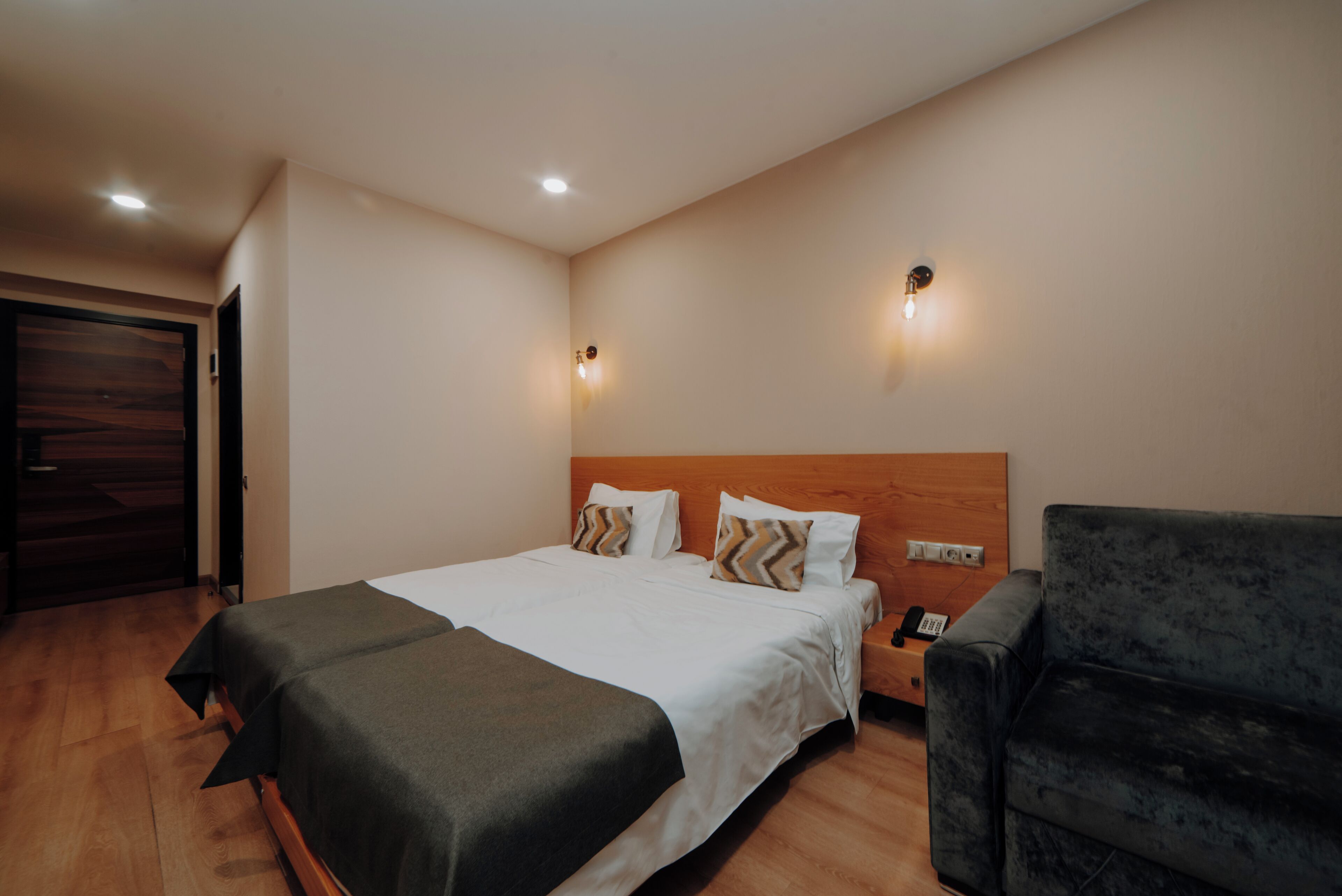 Habitación de hotel con cama, mesita de noche y sillón oscuro.