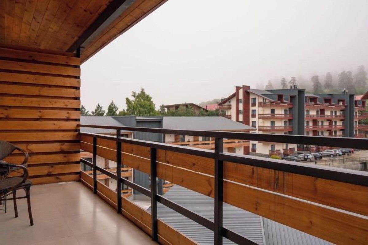 A wooden balcony with a view of buildings and a parking area.