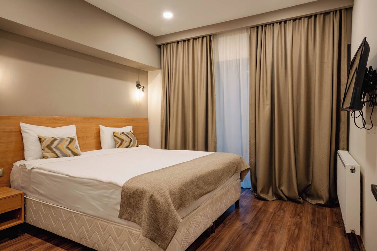 A neatly made bed with a wooden headboard, a bedside table, and a wall-mounted TV.