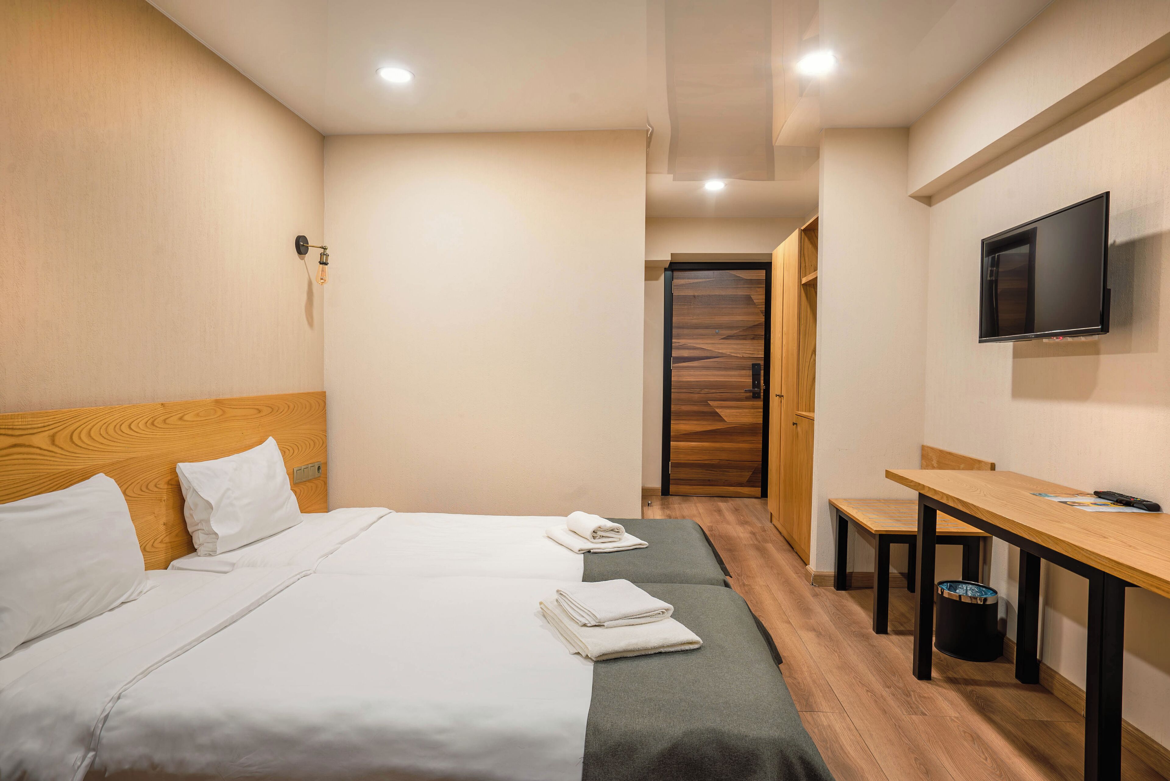 A hotel room with two beds, a wooden headboard, a TV mounted on the wall, and a small table with a chair.