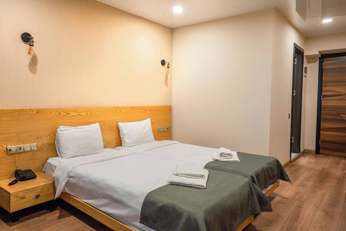 A hotel room with a wooden headboard, a single bed with white bedding, a bedside table with a phone, and a small drawer.