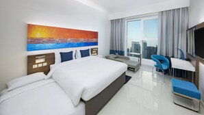 Une chambre d’hôtel moderne, dotée d’un grand lit, d’un bureau, d’une chaise et d’un tableau représentant un coucher de soleil sur l’océan.