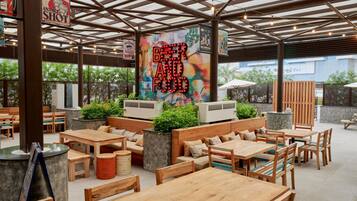 Un espace de restauration en plein air avec des tables et des bancs en bois, entouré de verdure et de climatiseurs.