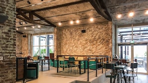 Un café spacieux aux murs en briques apparentes, doté de mobilier moderne et d’un escalier menant à un niveau supérieur.