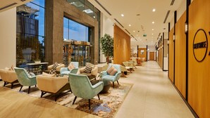 Un hall d’hôtel avec des espaces aménagés pour s’asseoir, un comptoir d’accueil et une grande fenêtre.