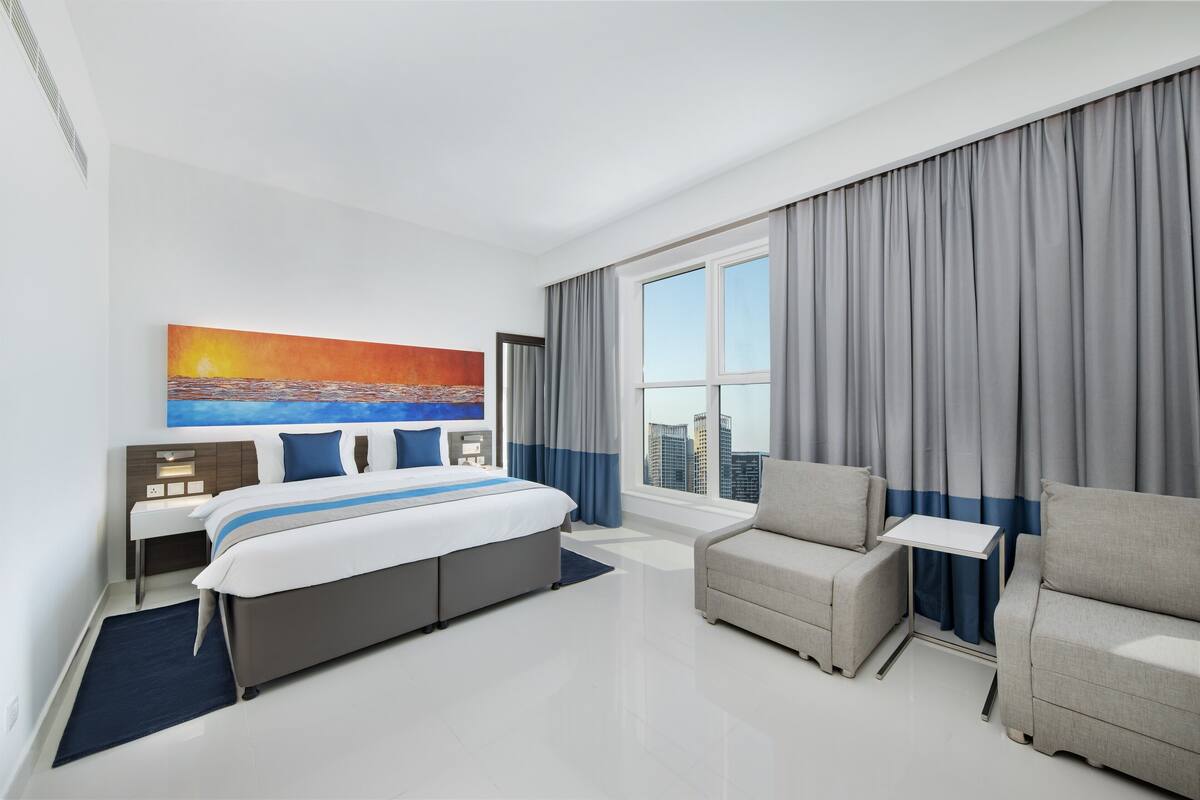 Une chambre d’hôtel moderne avec un grand lit, un canapé, une petite table et une vue sur la ville.