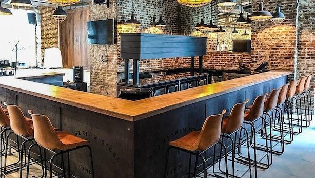 Un espace bar doté d’un long comptoir, de plusieurs suspensions décoratives et d’un mur en briques en arrière-plan.
