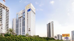 Un hôtel moderne de grande hauteur, reconnaissable à son grand panneau « CityMax », entouré d’une végétation luxuriante et d’autres immeubles de grande hauteur.