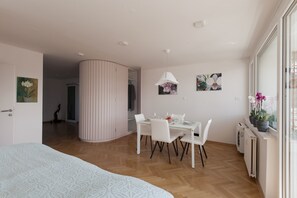 A modern bedroom with a large bed, a dining area with a table and chairs, and a view of the outdoors through a window.
