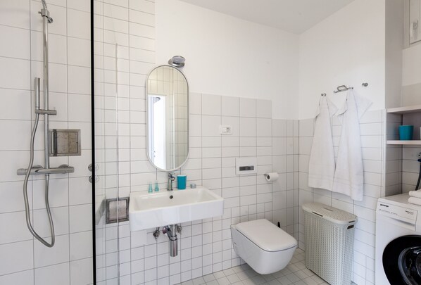 Un baño con ducha, lavamanos, inodoro y lavadora.