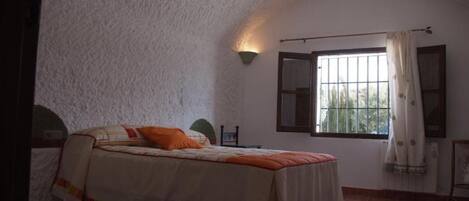 A bedroom with a bed, a window with curtains, a wall-mounted light, and a radiator.