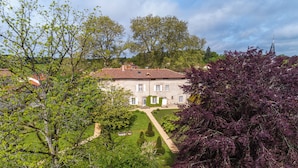 Un grand bâtiment en pierre, doté d’une façade symétrique, d’une entrée centrale et d’un jardin bien entretenu, avec un chemin menant à l’entrée.